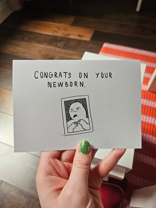 Hand holding a card with 'Congrats on your newborn' text and a baby illustration.