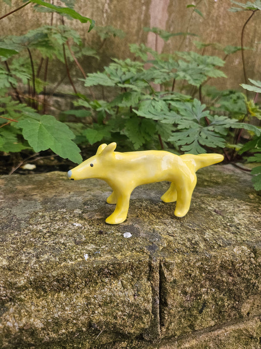A small glossy yellow dog figurine mounted on a textured stone wall outdoors, with green leaves visible in the background.